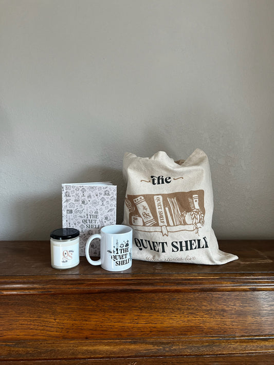 Tote bag, mug, candle, and journal on a wooden surface with a neutral background