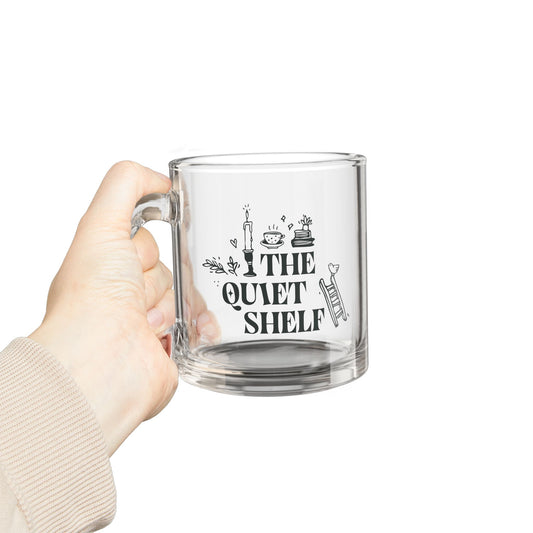 Clear mug with 'The Quiet Shelf' design held by a hand on a white background