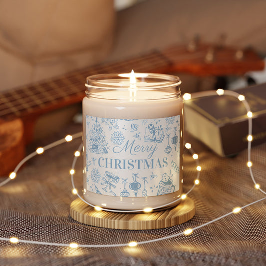 Candle with a 'Merry Christmas' label on a wooden coaster surrounded by string lights and a guitar in the background.
