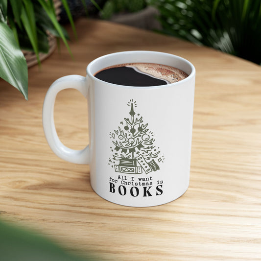 White mug with a Christmas tree design and 'All I want for Christmas is books' text on a wooden table.