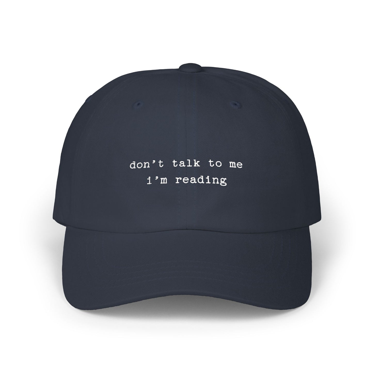 Navy blue cap with 'don't talk to me I'm reading' text on a white background