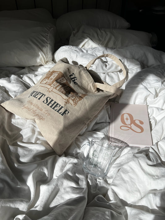 Beige tote bag with text and a notebook on a white bedspread