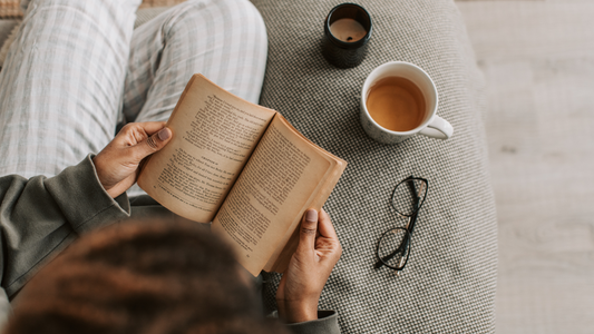 Cozy morning reading scene with open book, cup of tea, candle, and reading glasses