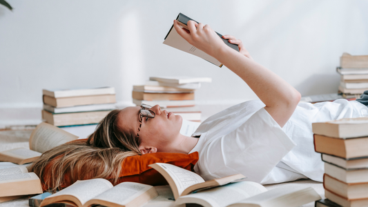 Woman reading on the floor surrounded by stacks of books.