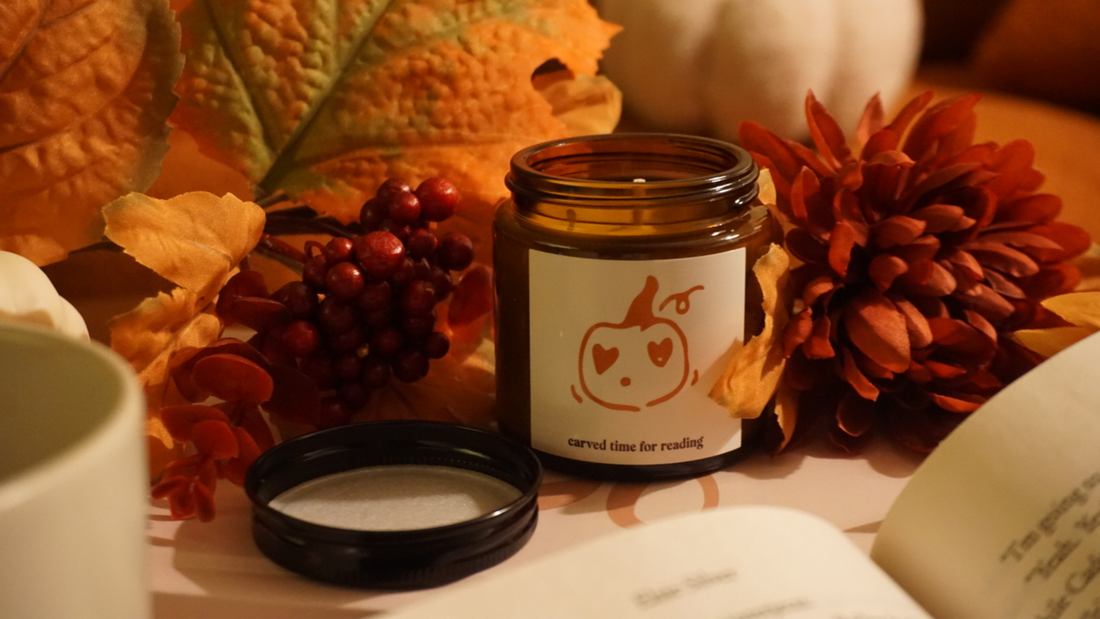 Amber jar candle with pumpkin design and “carved time for reading” label, styled with fall leaves, berries, and an open book.