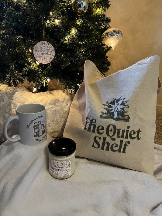 Decorative items including a mug, candle, and 'the Quiet Shelf' bag in front of a Christmas tree.