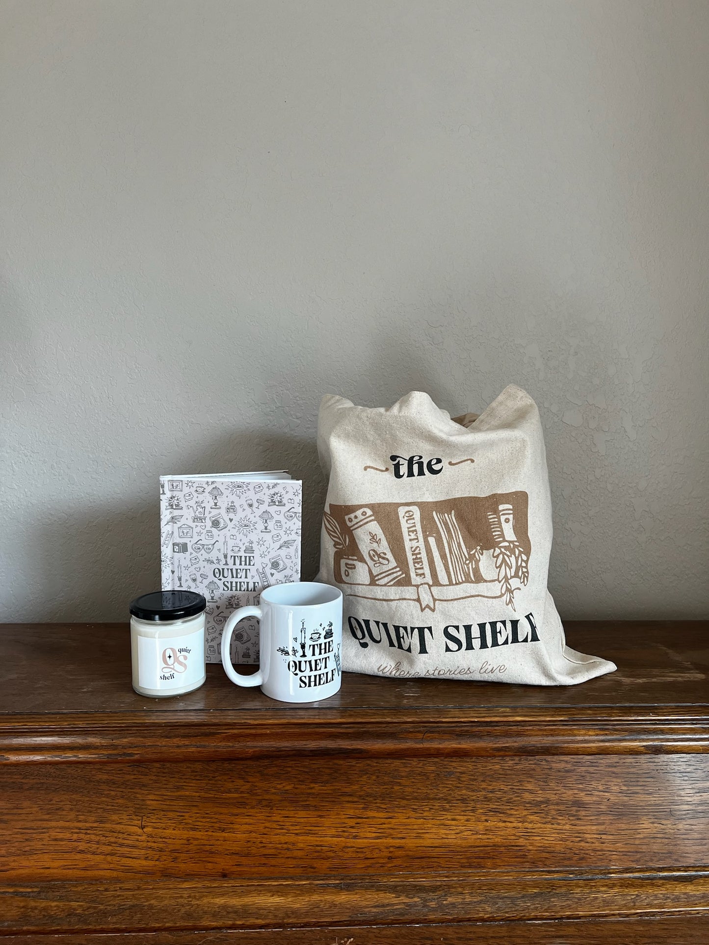 Tote bag, mug, candle, and journal on a wooden surface with a neutral background