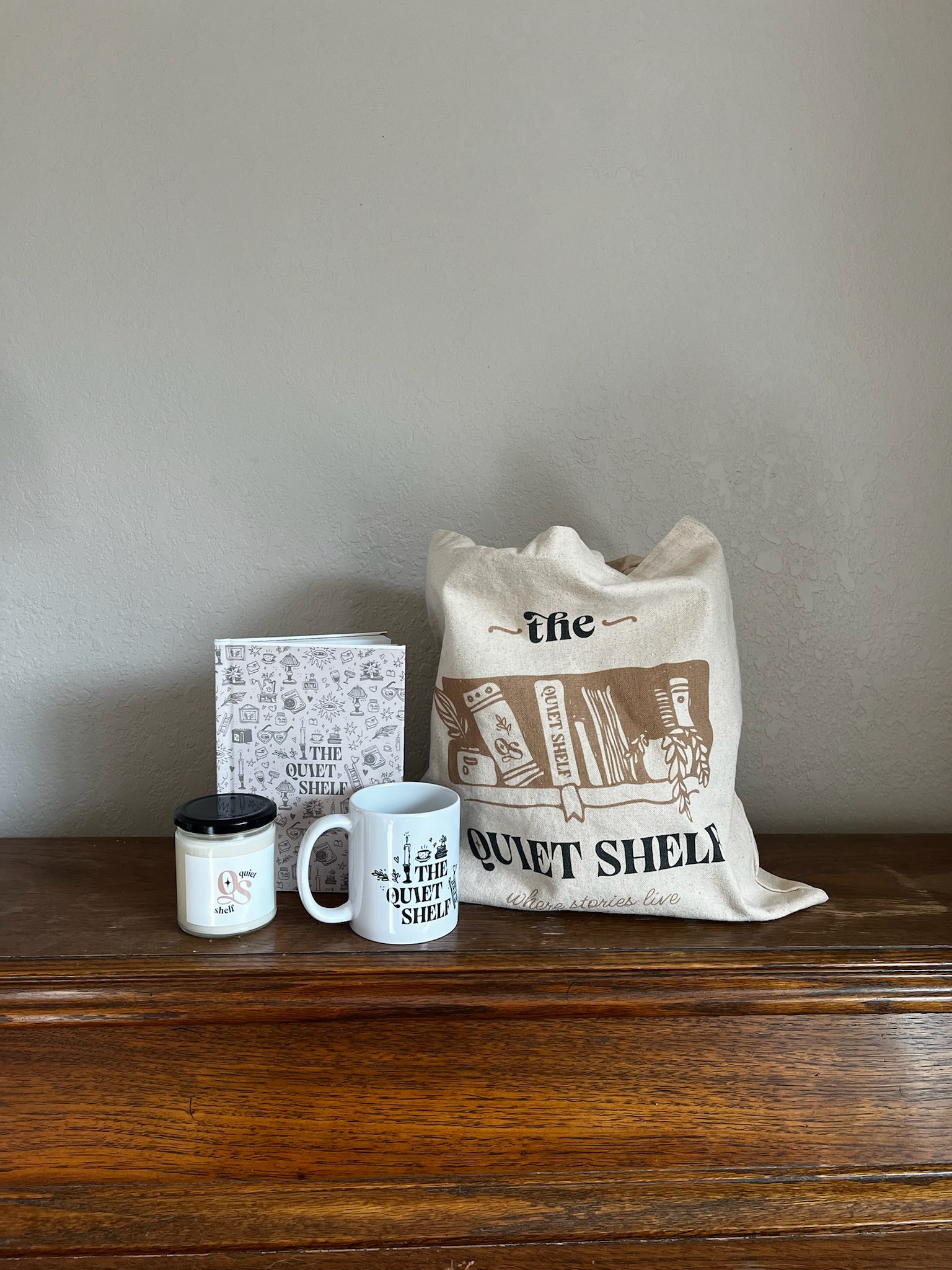 Tote bag, mug, candle, and journal on a wooden surface with a neutral background