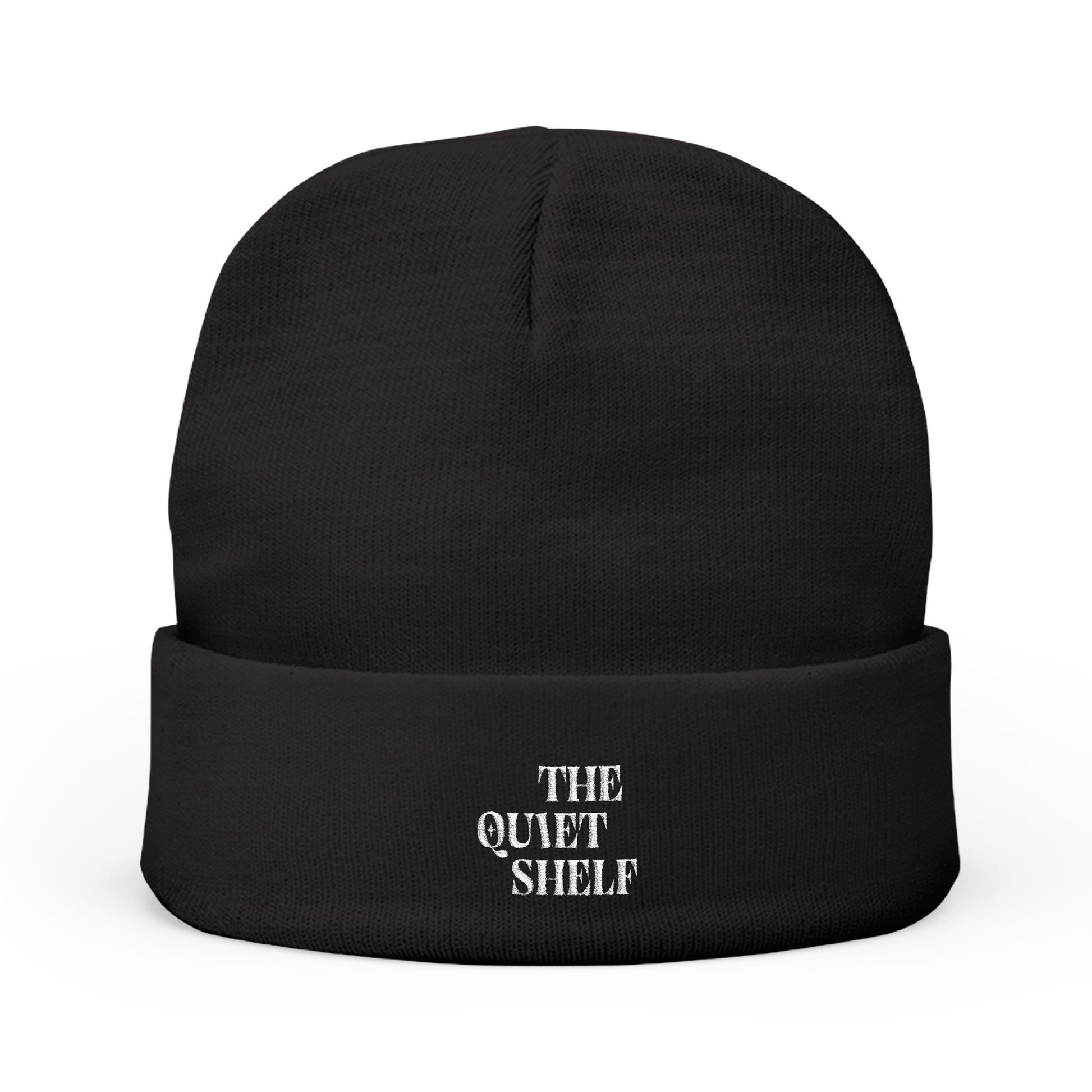 A black cuffed beanie with 'THE QUIET SHELF' embroidered in white on the fold-over cuff.