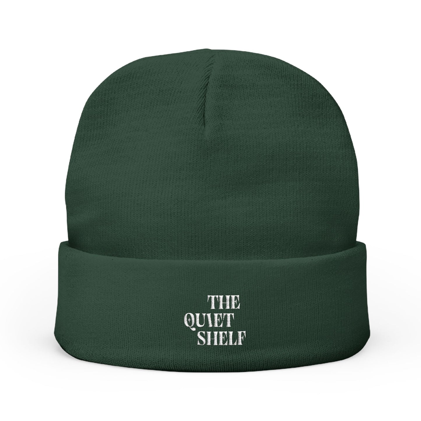 A green cuffed beanie with 'THE QUIET SHELF' embroidered in white on the fold-over cuff.