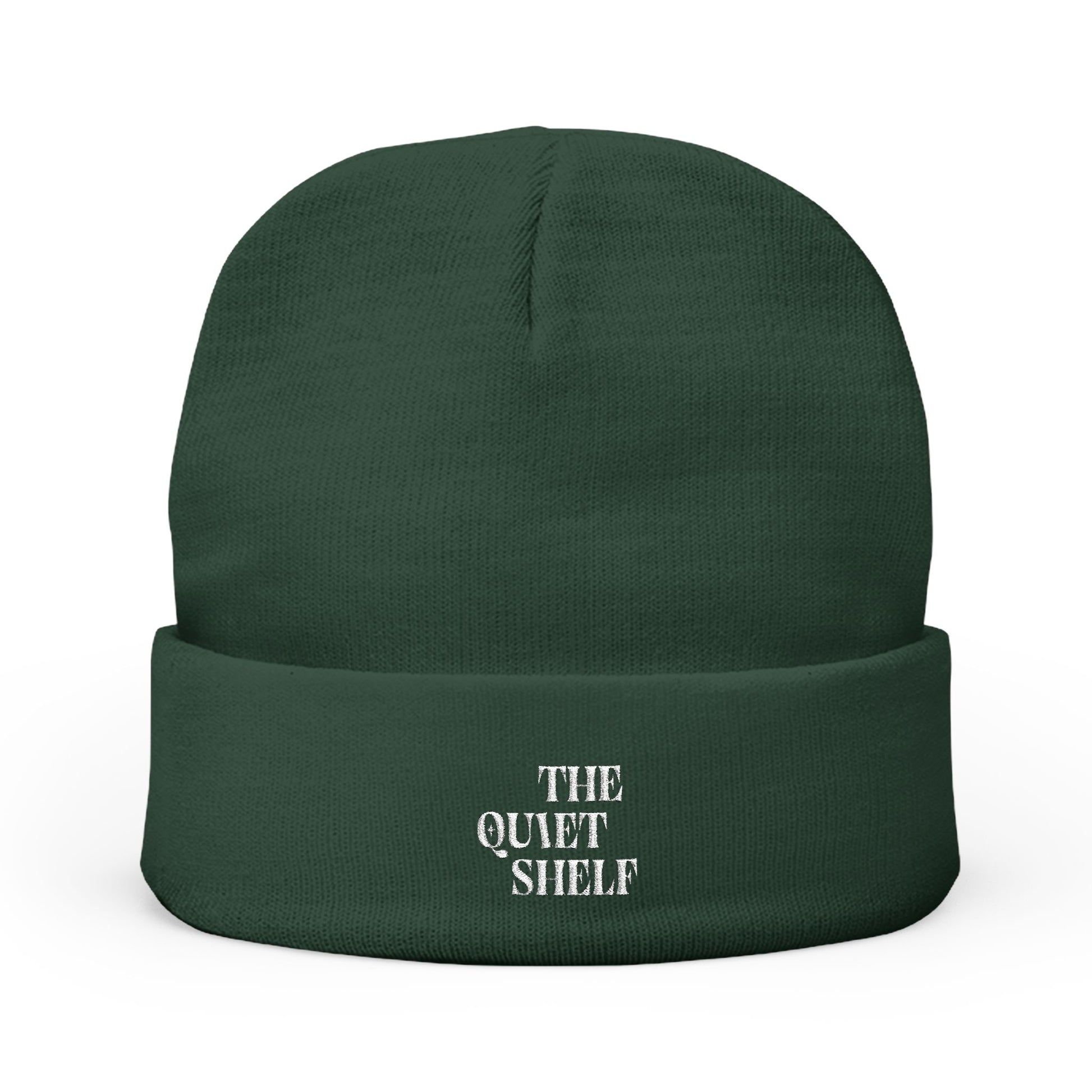 A green cuffed beanie with 'THE QUIET SHELF' embroidered in white on the fold-over cuff.
