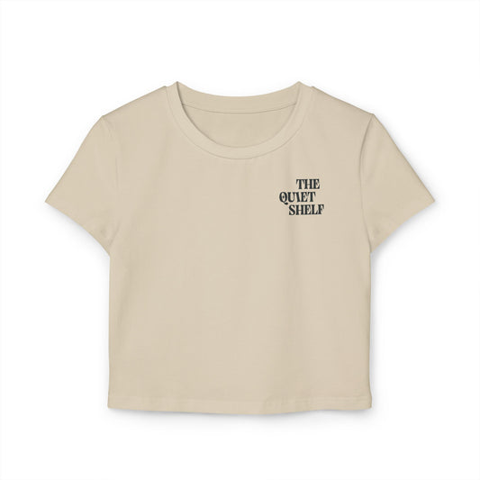 A beige cropped tee with 'THE QUIET SHELF' logo printed on the upper left chest area.