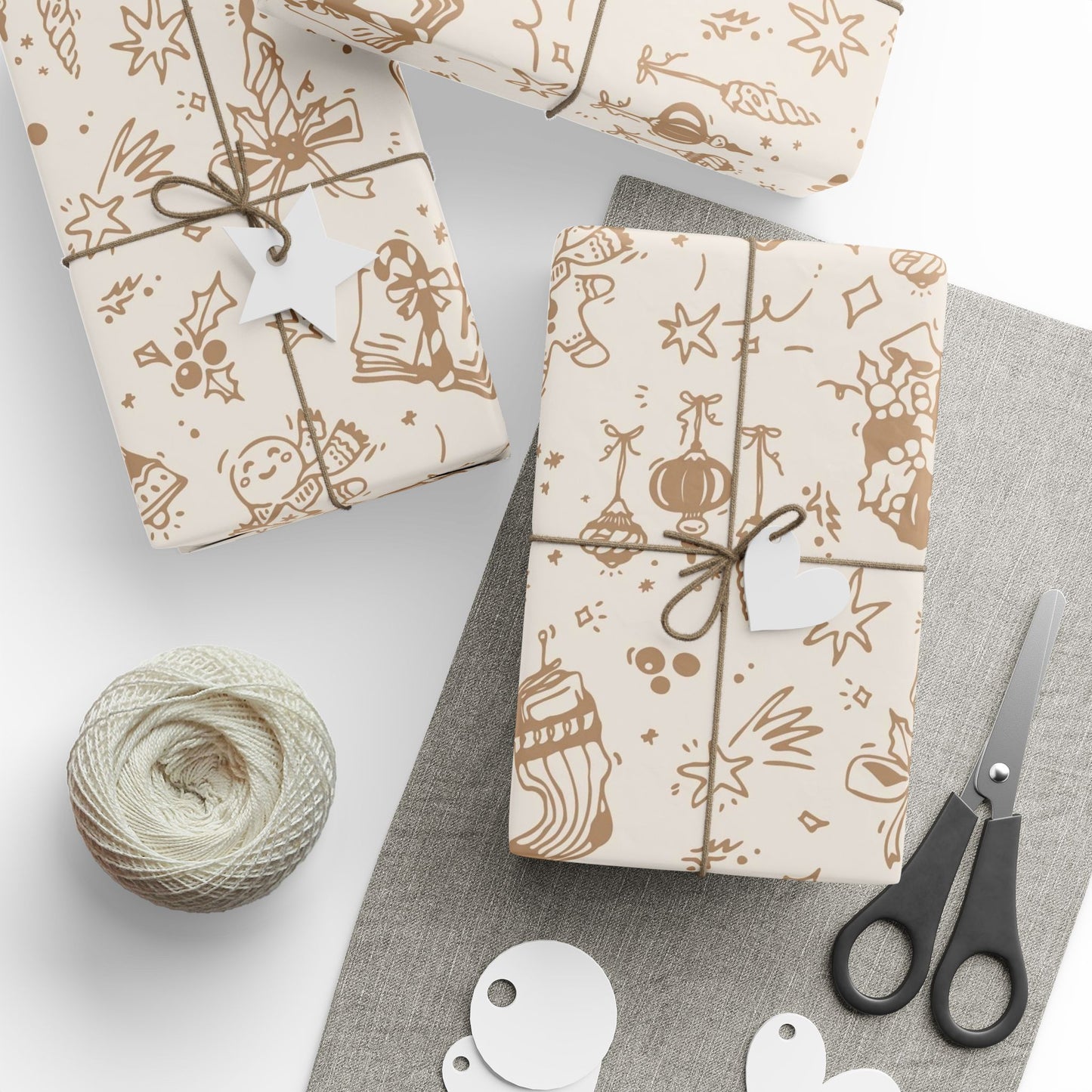 Gift wrapping paper with festive designs, scissors, and yarn on a gray surface.