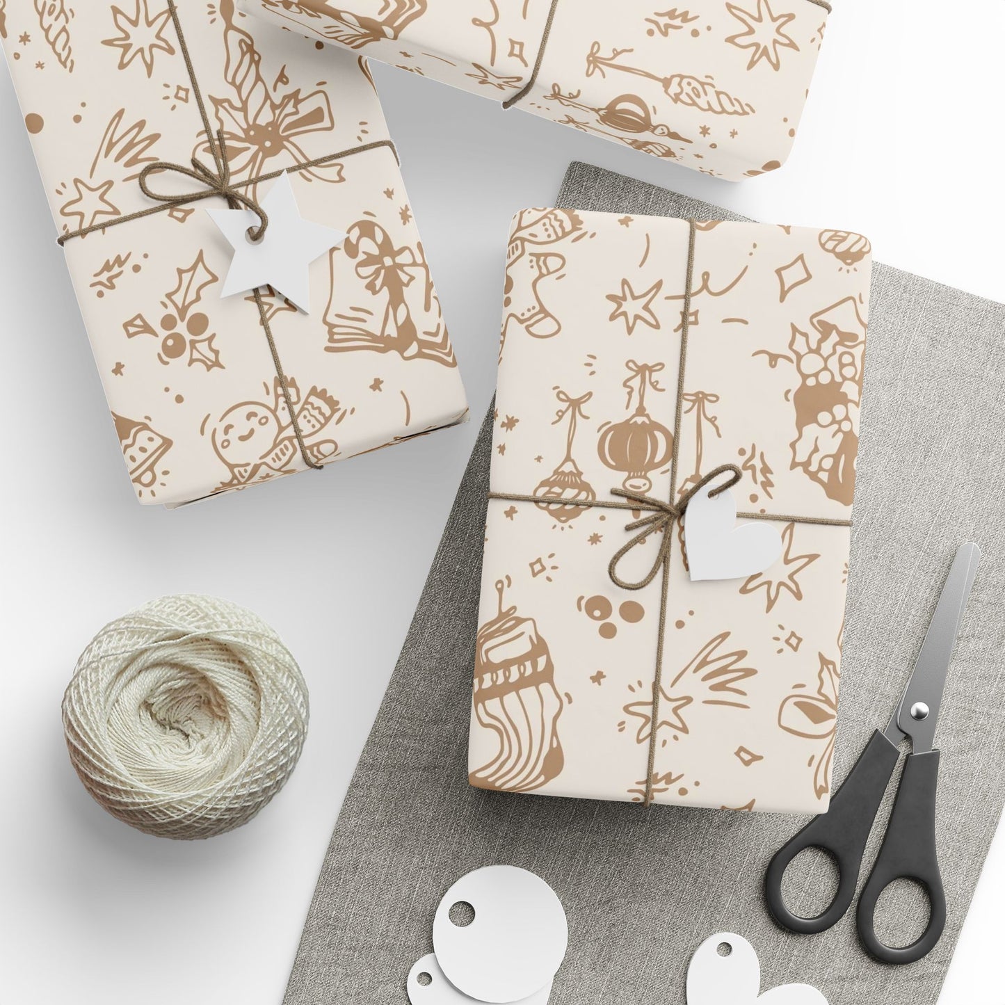 Gift wrapping paper with festive designs, scissors, and yarn on a white surface