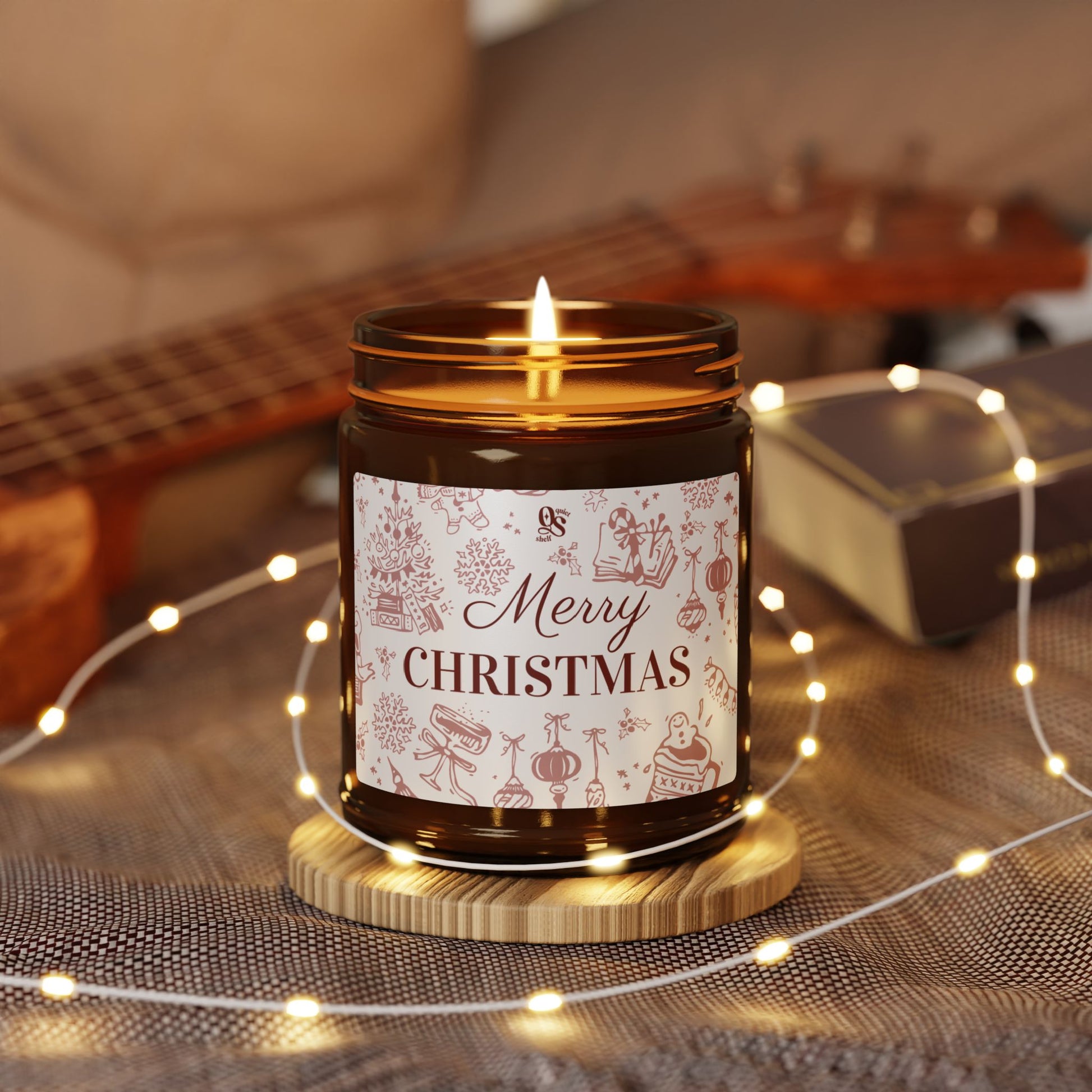 Candle with 'Merry Christmas' label on a wooden coaster surrounded by string lights and a guitar in the background.