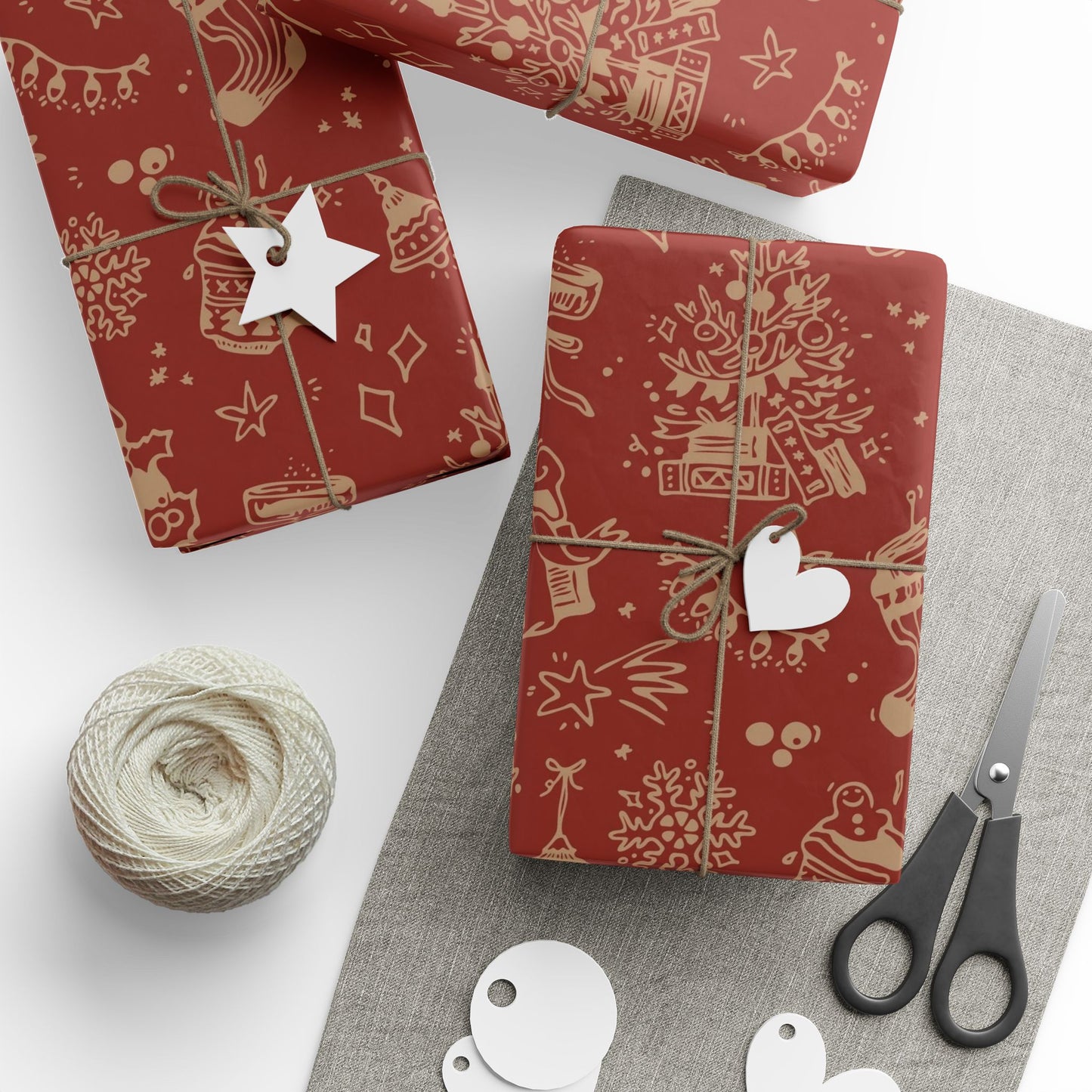 Red gift wrap with Christmas designs, scissors, and yarn on a white surface