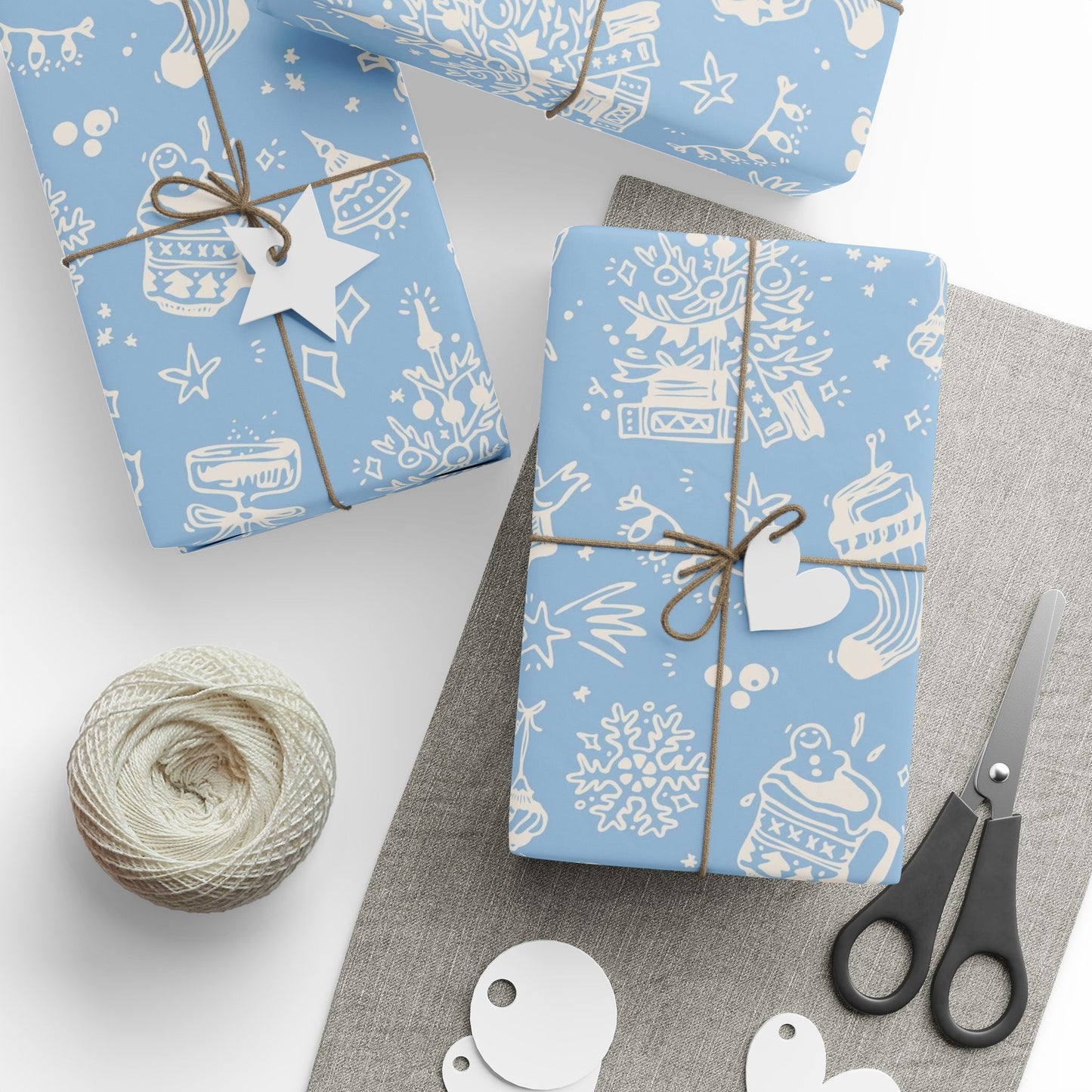 Gift boxes wrapped in blue paper with white patterns, tied with string, on a white surface with scissors and yarn.