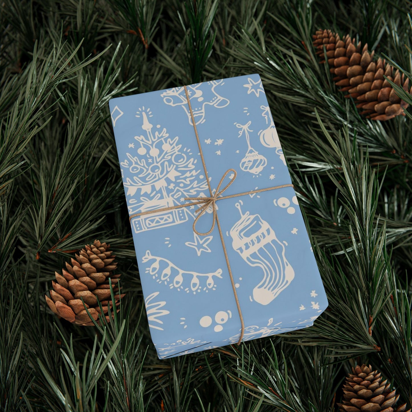 Blue wrapped gift with white designs on a bed of pine needles and pine cones