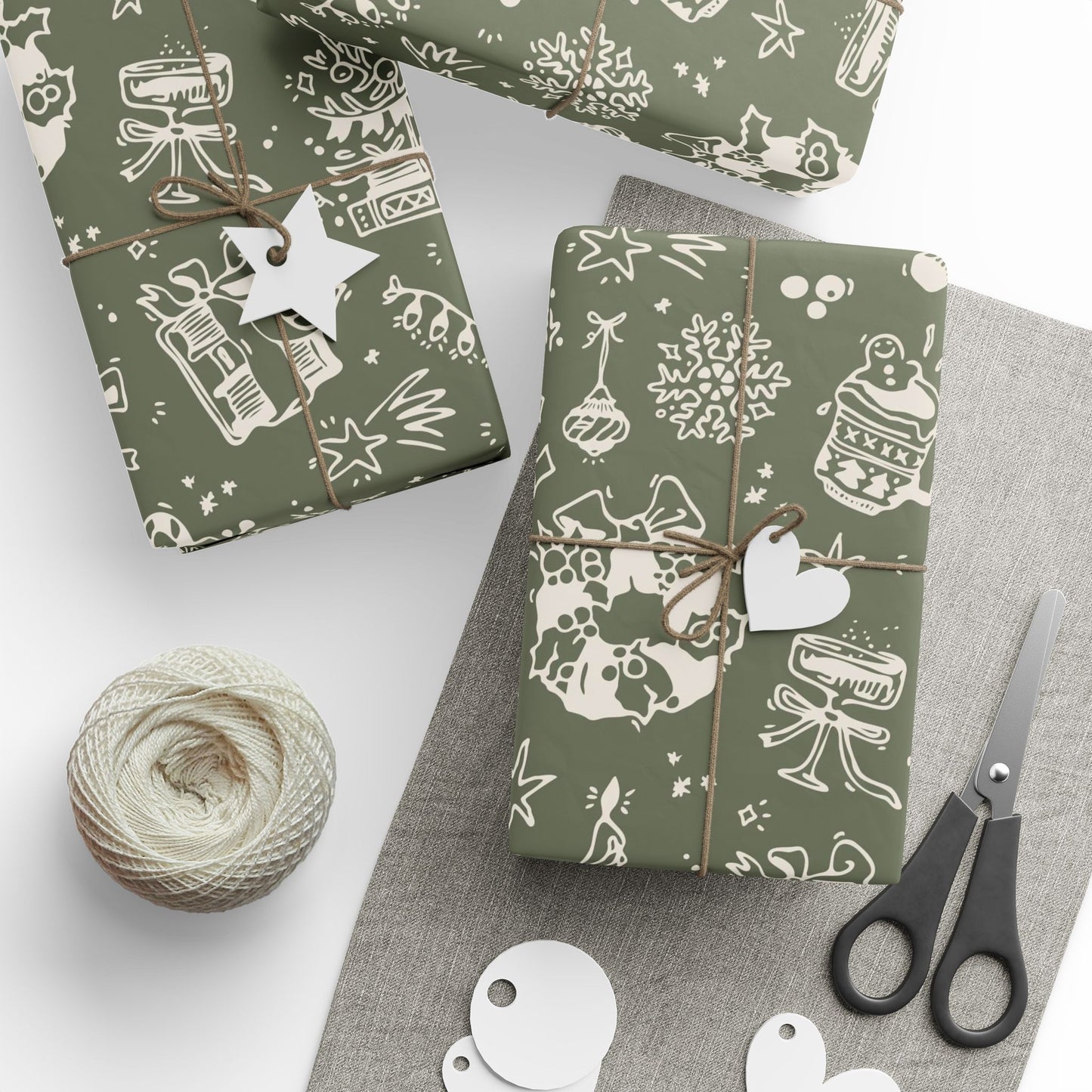 Gift boxes wrapped in green paper with white patterns, scissors, and yarn on a gray surface.