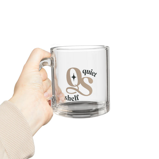 Clear glass mug with 'QS' logo and text held by a hand on a white background