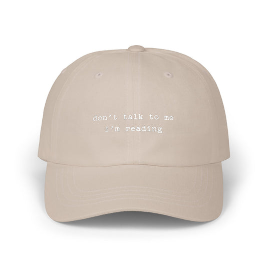 Beige cap with 'don't talk to me I'm reading' text on a white background
