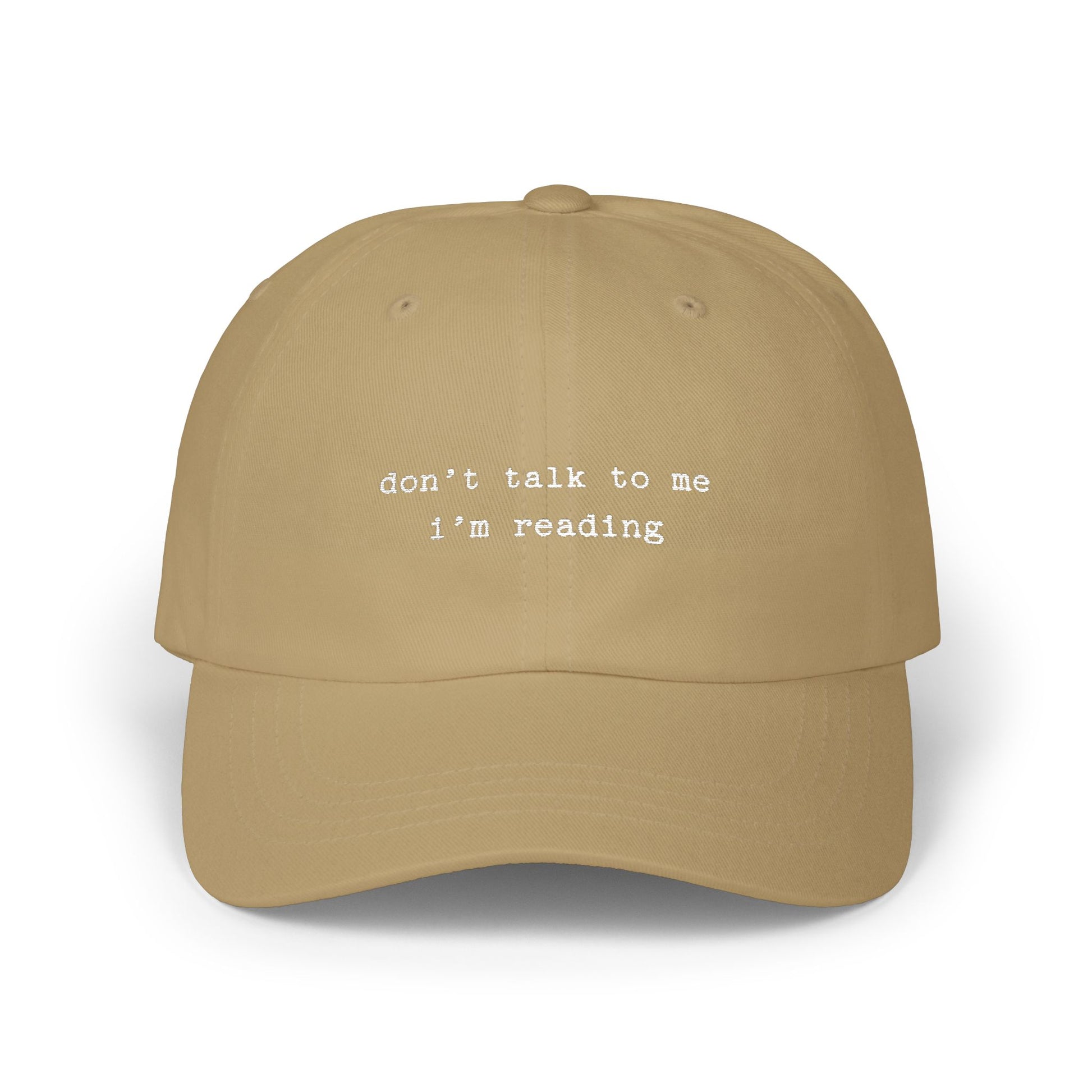 Beige cap with 'don't talk to me I'm reading' text on a white background