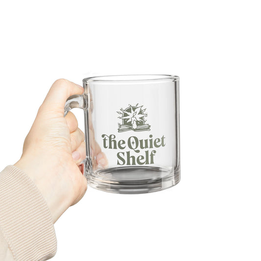 Clear mug with 'the Quiet Shelf' logo held by a hand on a white background