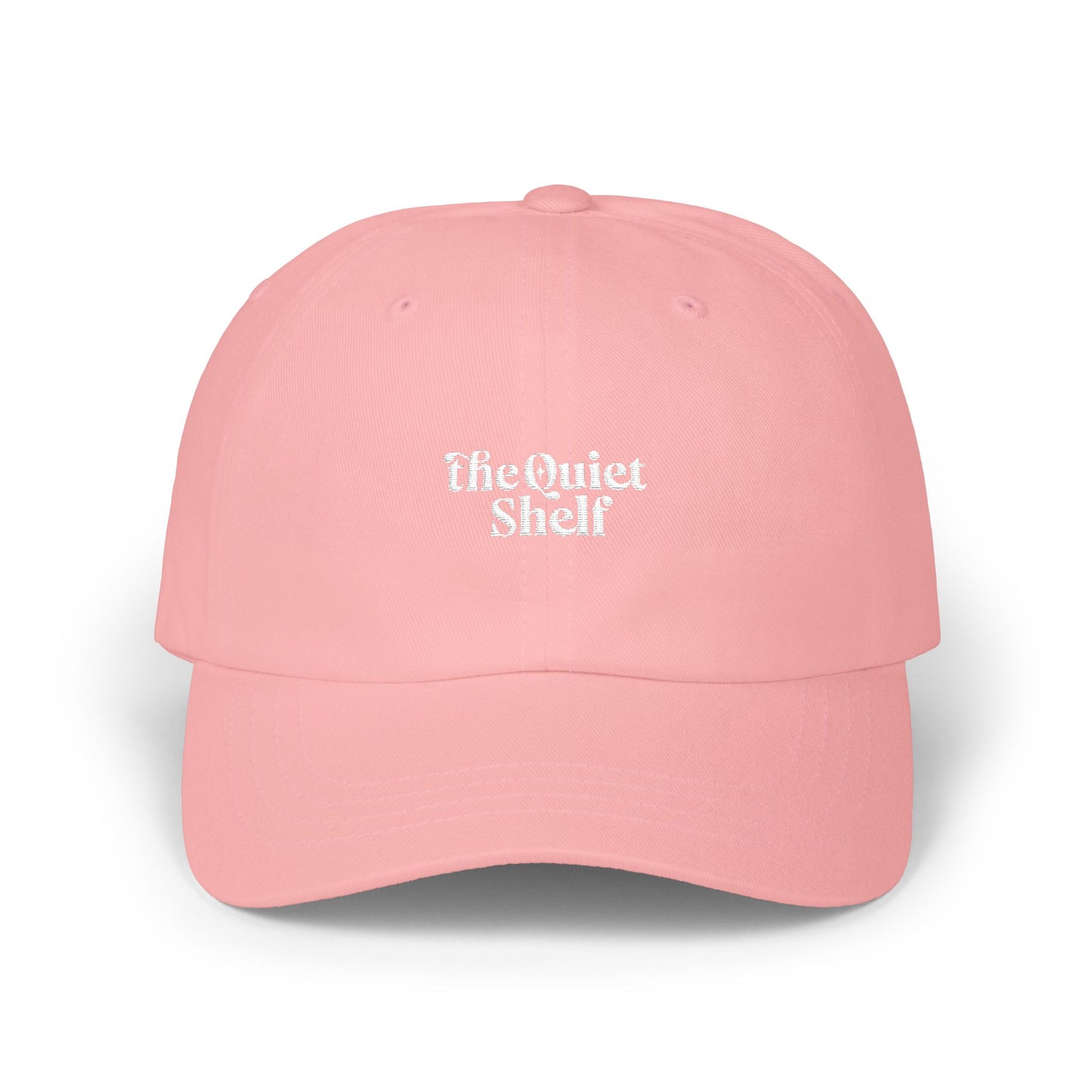 A pink dad hat with 'The Quiet Shelf' logo embroidered in the center.