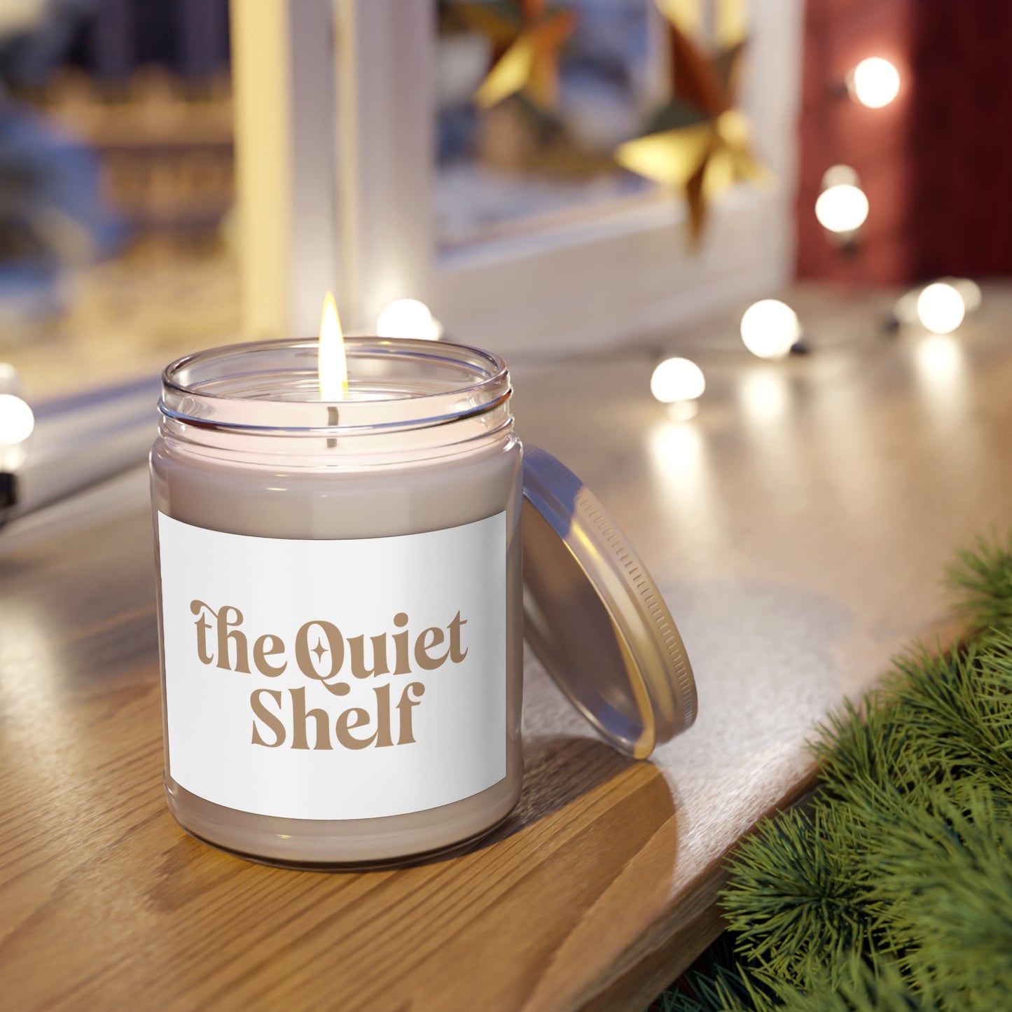 Candle in a jar labeled 'the Quiet Shelf' on a wooden surface with blurred lights in the background