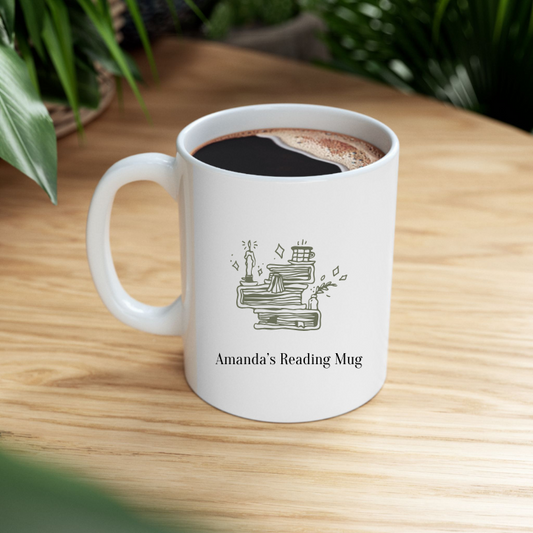A white ceramic mug with a personalized name 'Amanda's Reading Mug' printed on the front, featuring a quiet shelf icon and book illustrations, on top of a wooden table