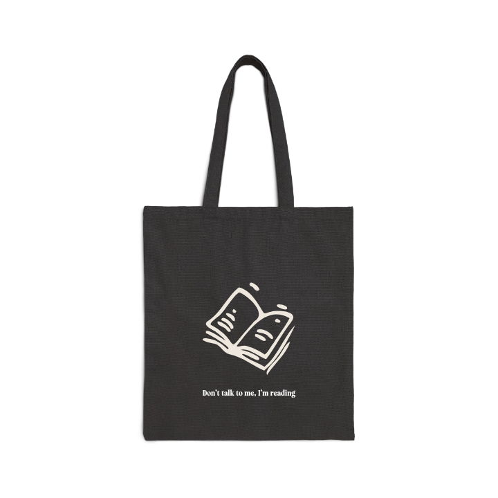 A black tote bag with an open book icon plus 'Don't talk to me, I'm reading' text on it