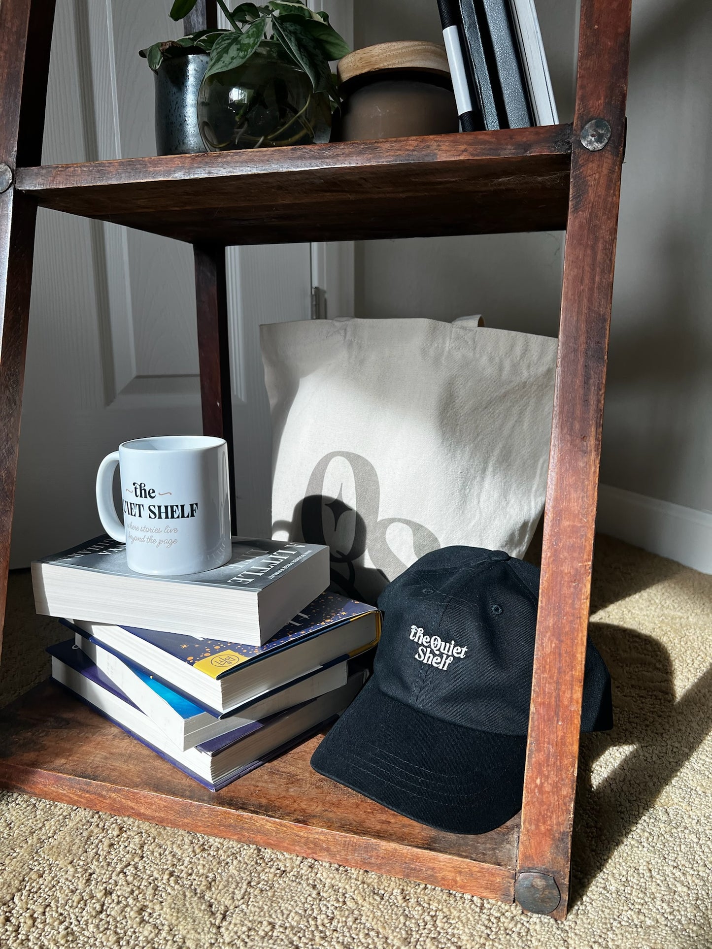 Stack of books with a mug, cap, and tote bag on a wooden shelf.