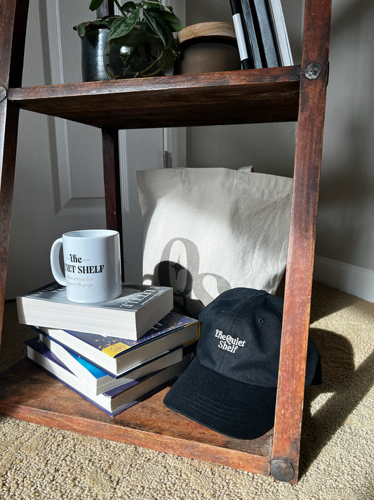 Stack of books with a mug, cap, and tote bag on a wooden shelf.