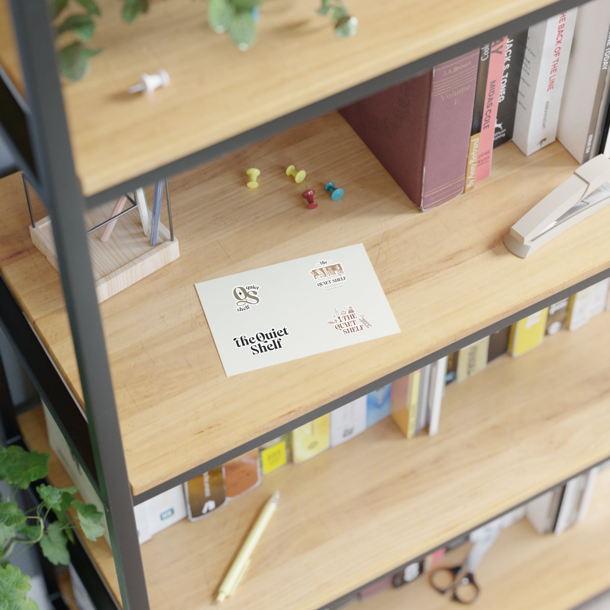 Four vinyl stickers with different designs, each featuring The Quiet Shelf's branding, on a bookshelf