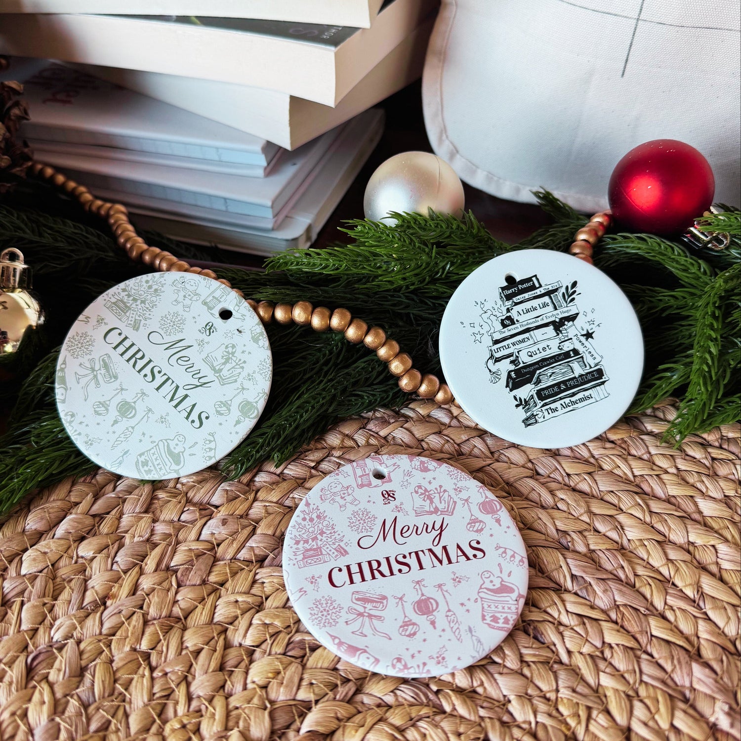 Three round Christmas ornaments with 'Merry Christmas' text on a woven surface with festive decorations.